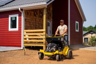 Man operating mini skid steer near red barn.