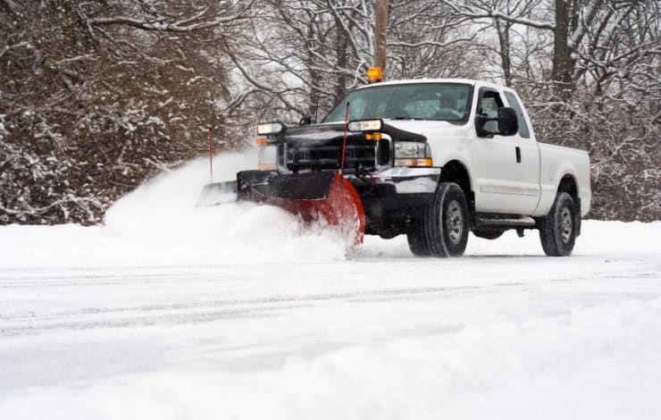 Snow plow truck clearing road during winter storm.